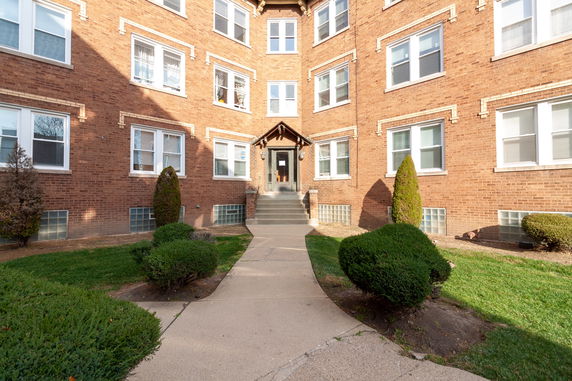 Front view of a multi-story brick apartment building with multiple windows and a central entrance.