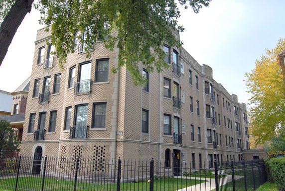 Front view of a four-story brick apartment building with multiple windows and a gated entrance.