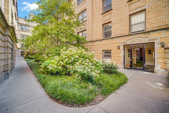 Front view of a building entrance with a garden and sidewalk.