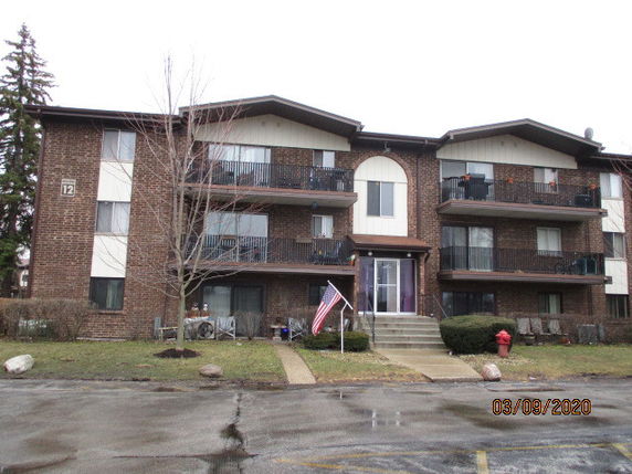 Front view of a three-story brick apartment building with balconies.