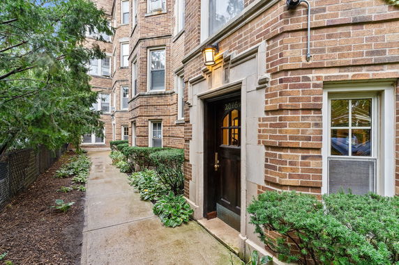 Front view of a brick building entrance with a pathway and greenery.