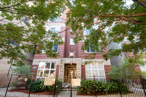 Front view of a multi-story brick building with large windows and a gated entrance.