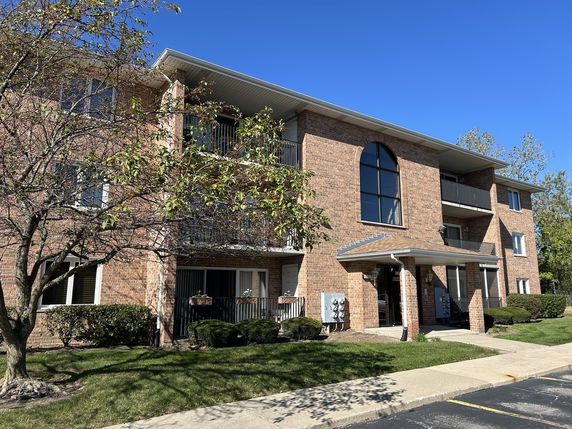 Front view of a three-story brick apartment building with balconies.