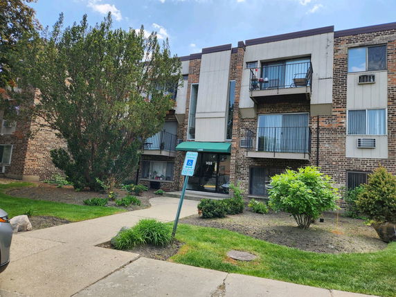 Front view of a multi-story brick apartment building with balconies and greenery.