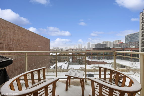 Snow-covered balcony with wooden chairs overlooking city buildings.