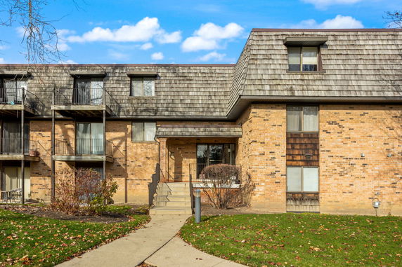 Front view of a multi-story brick building with balconies and shingle roofing.