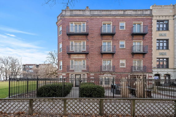 Front view of a multi-story brick building with balconies and a fenced entrance.