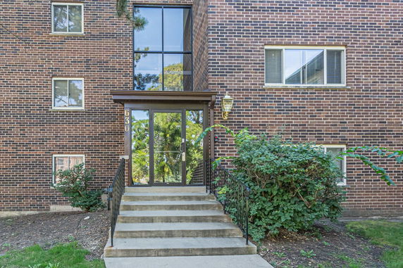Front view of a brick apartment building with glass entrance and stairs.