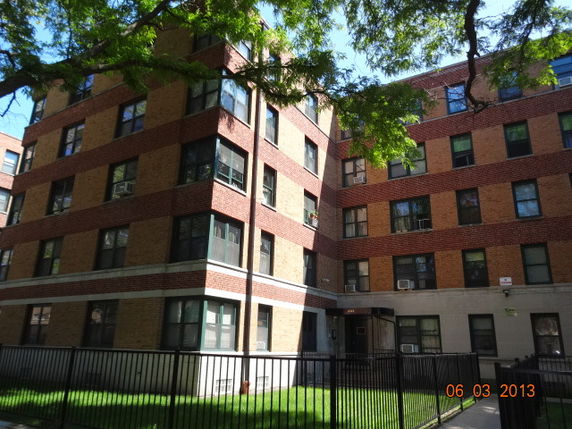 Front view of a multi-story brick apartment building with fenced area.