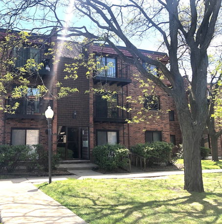 Front view of a multi-story brick apartment building with balconies and a single entrance.