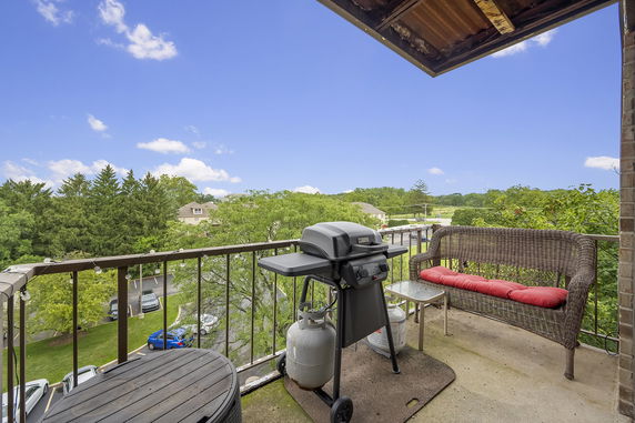 Outdoor balcony with a grill, seating, and a view of the surrounding greenery.