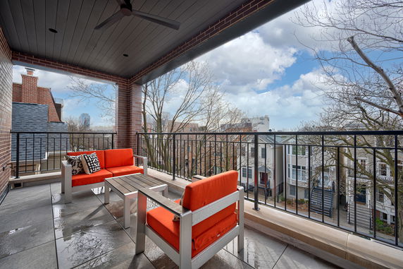 View from a balcony with seating area, overlooking residential buildings and trees.