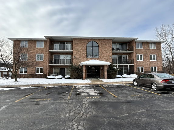 Front view of a three-story brick apartment building with balconies.
