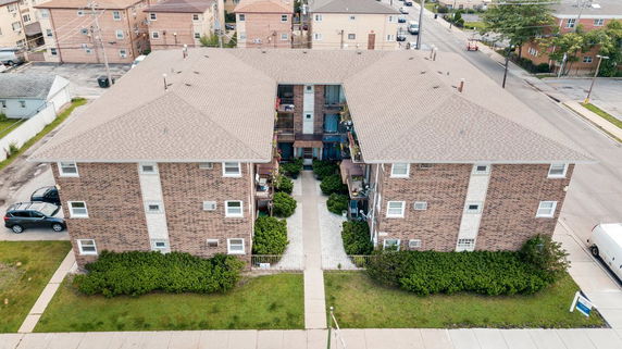 Front view of a multi-story brick apartment building with a central entrance and parking areas on the sides.