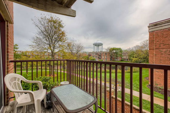 View from a balcony overlooking a grassy area with trees and a water tower in the distance.