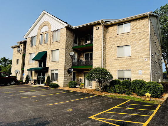 Front view of a multi-story brick apartment building with several awnings and satellite dishes.