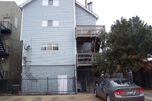 Side view of a multi-story residential building with a balcony and adjacent car.