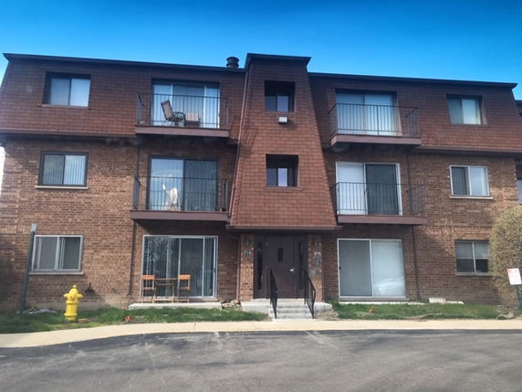 Front view of a three-story brick apartment building with balconies.