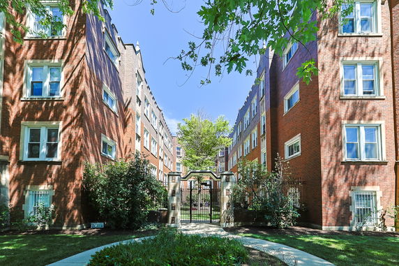 Front view of a multi-story brick apartment building with a gated entrance.