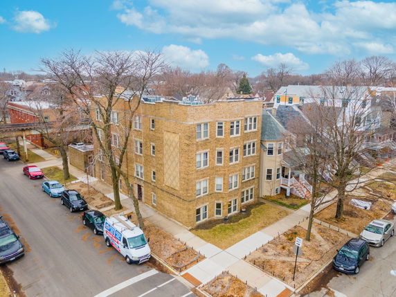 Front view of a three-story apartment building on a street corner with cars parked along the road.