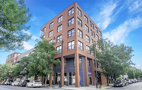 Front view of a multi-story brick building with large windows and retail space on the ground floor.