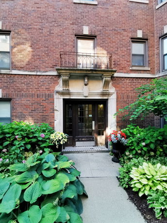 Front view of a brick building entrance with decorative plants.