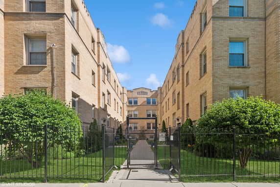 Front view of a multi-story brick apartment building with gated entrance.