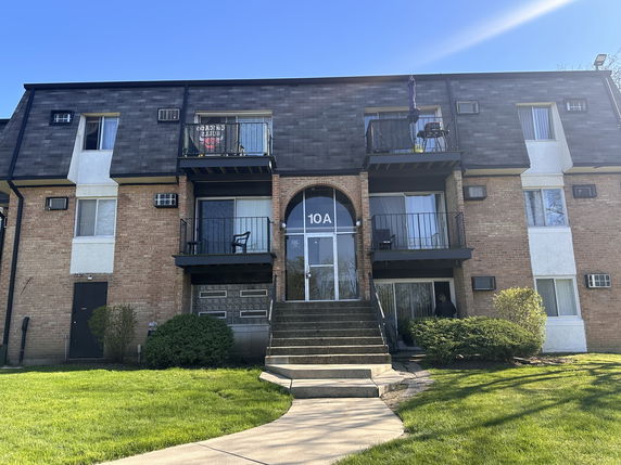 Front view of a multi-story apartment building with balconies and brick exterior.