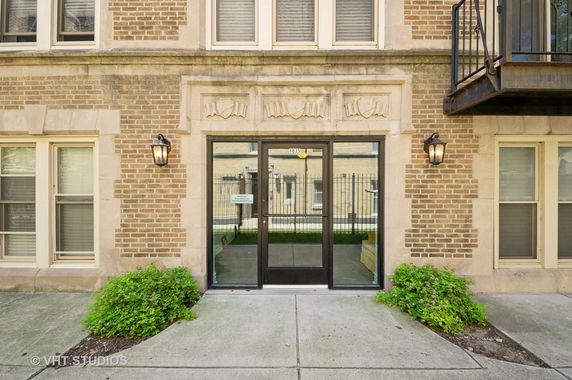 Front view of a brick apartment building entrance with decorative stonework and glass door.