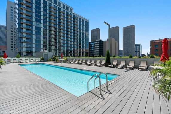 Outdoor swimming pool on a rooftop with lounge chairs and city buildings in the background.