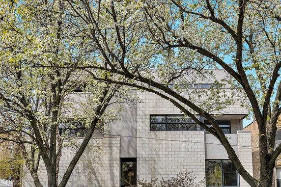Front view of a modern multi-story house with large windows and white brick exterior.