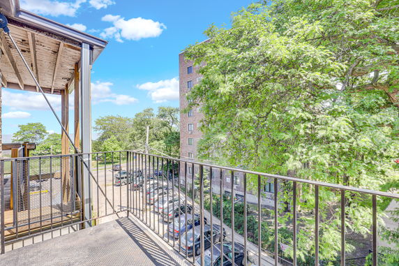 Panoramic view from a balcony overlooking a parking area and trees.