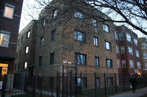 Front view of a multi-story brick apartment building with a fenced yard.