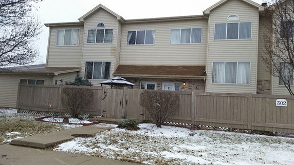 Front view of a two-story residential building with multiple windows and a fenced yard.