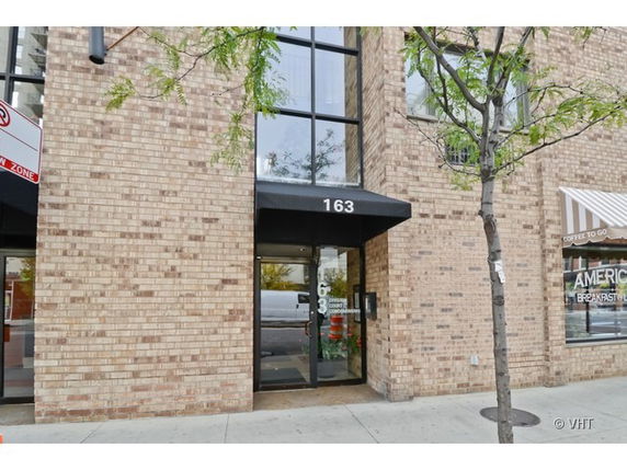 Front view of a brick building with a glass entrance and black awning labeled 163.