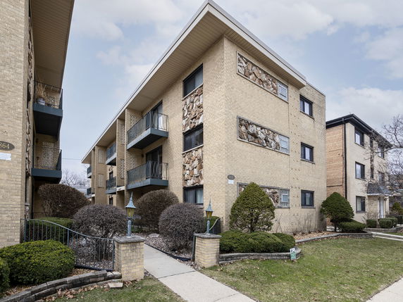 Front view of a multi-story apartment building with balconies and brick exterior.