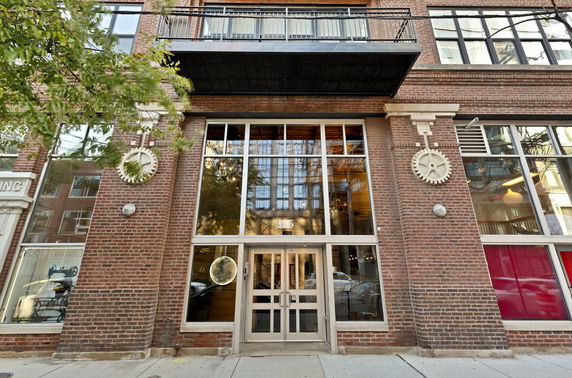 Front view of a multi-story brick building with large windows and a metal balcony.