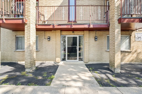 Front view of a brick building entrance with a glass door and balcony above.
