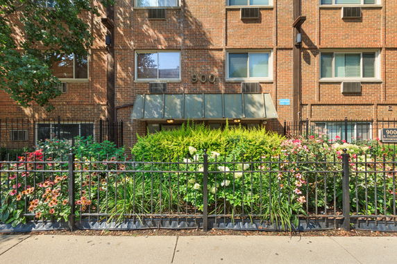 Front view of a brick building with metal awning and surrounding garden.