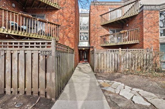 Front view of a brick apartment building with balconies and a wooden fence.