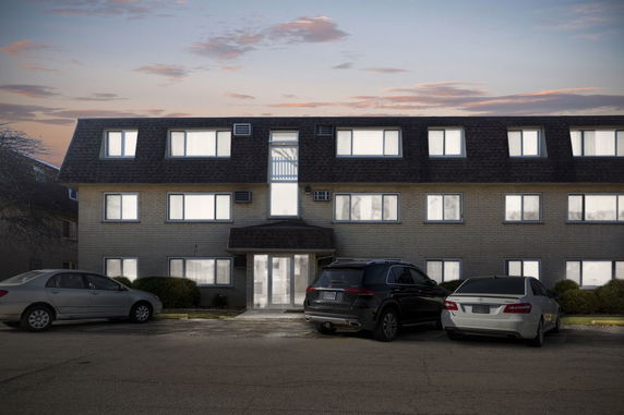 Front view of a three-story apartment building with a sloped roof and parked cars in front.