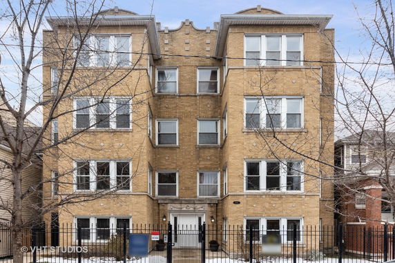 Front view of a multi-story brick apartment building with several windows and a gated entrance.
