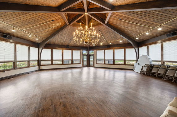 Large indoor space with wooden ceiling and floor, featuring a central chandelier.