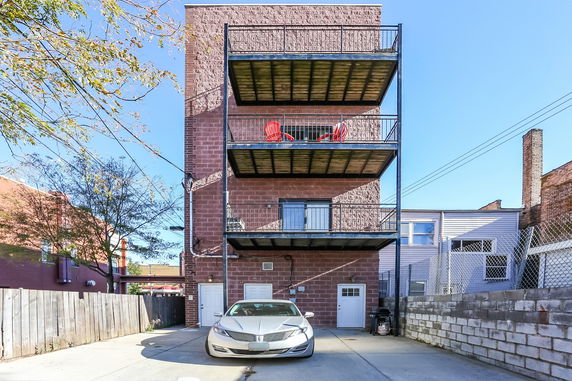 Front view of a multi-story brick building with balconies and a parked car.