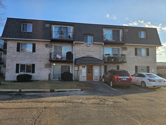 Front view of a three-story apartment building with a shingled roof and balconies.