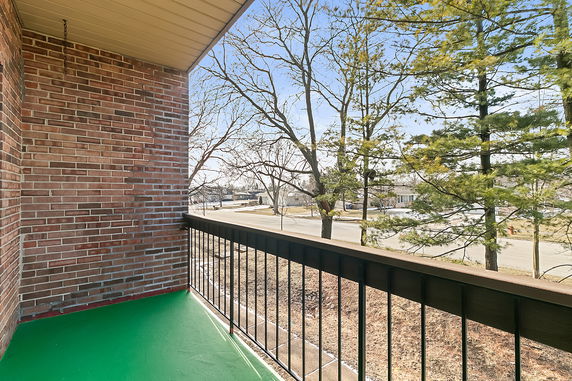 View from a balcony with brick walls and metal railing, overlooking trees and a street.