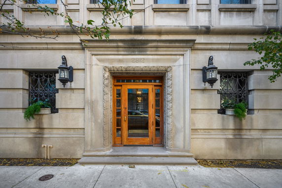 Front view of a stone building entrance with wooden double doors and decorative trim.