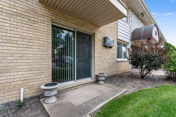 Front view of a building with a sliding glass door and adjacent windows, featuring beige brick and white siding.