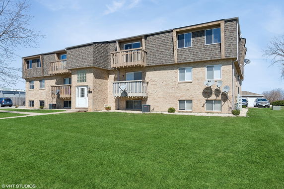 Front view of a two-story brick apartment building with balconies and satellite dishes.