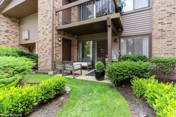 View of a brick and siding exterior of a two-story residential building with a balcony and ground-level patio.